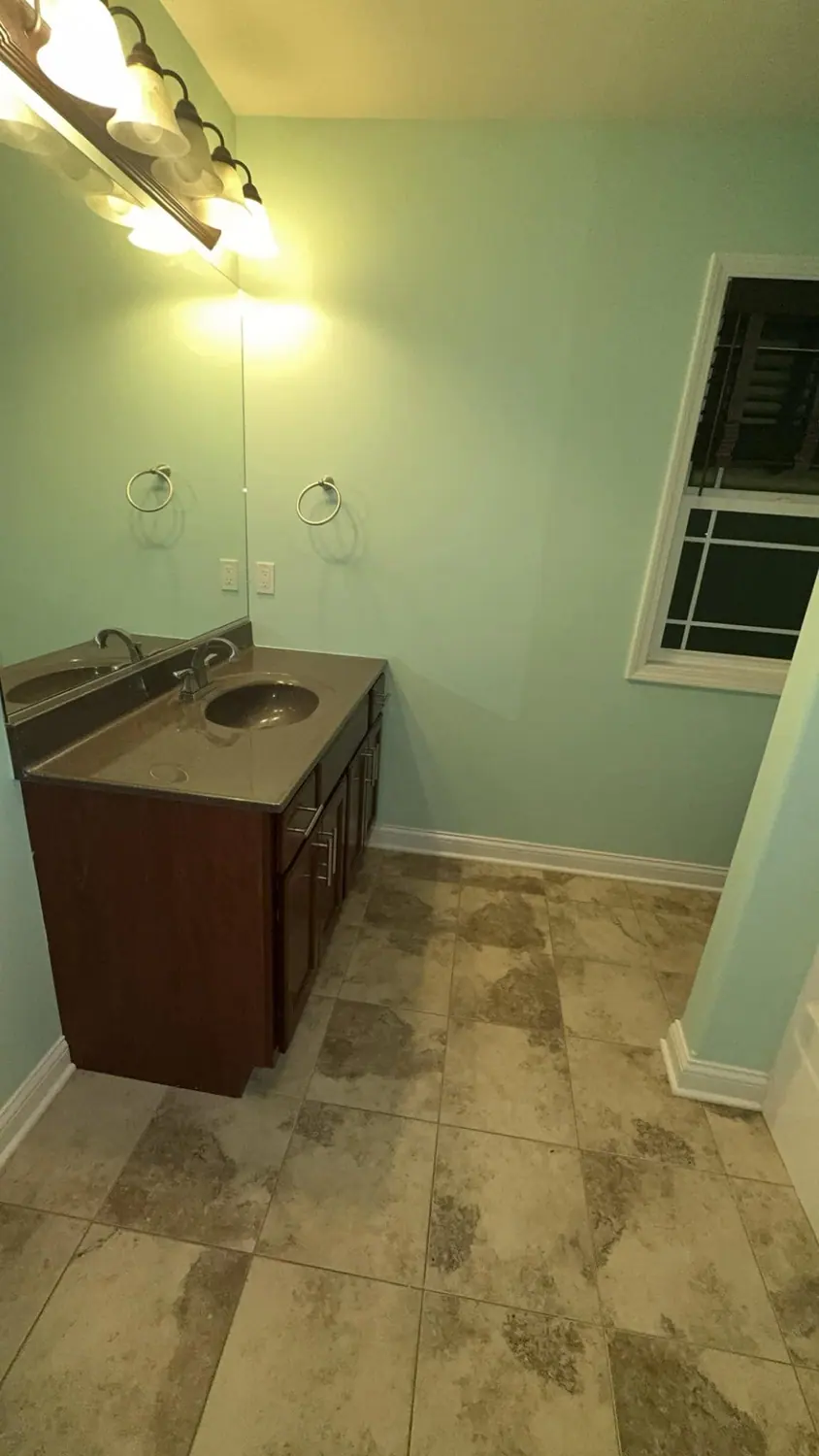 Wood vanity and stone floor cleaned in a green bathroom